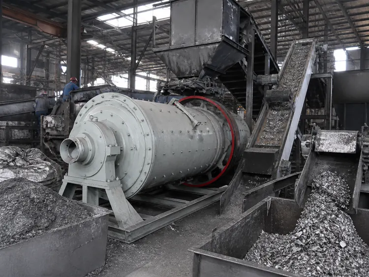 Gray ball mill beside inclined conveyors and bins of metallic residue in a recycling workshop
