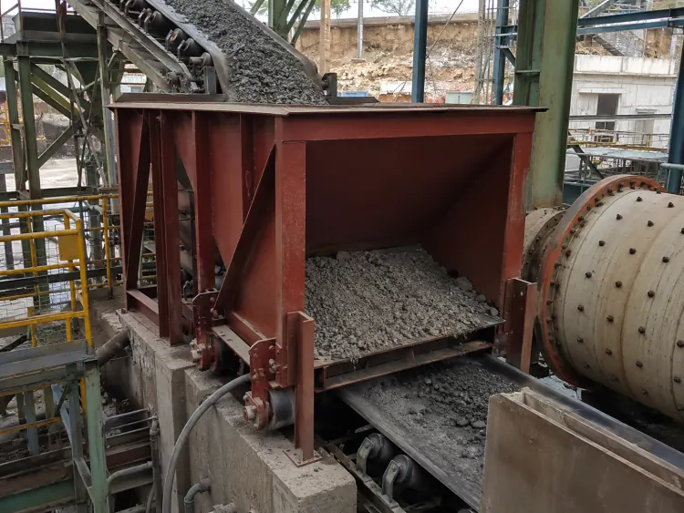 Front view of a red-brown chute feeder filled with gray ore beside a ball mill