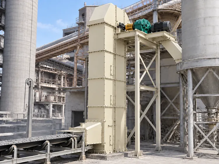 Cream bucket elevator with an upper motor platform beside cement plant silos and conveyors