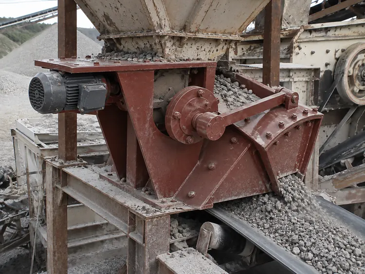 Red-brown feeder containing coarse gray rock above a belt conveyor