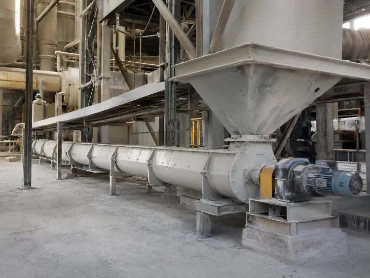 Horizontal enclosed screw conveyor beneath a large hopper inside a cement plant