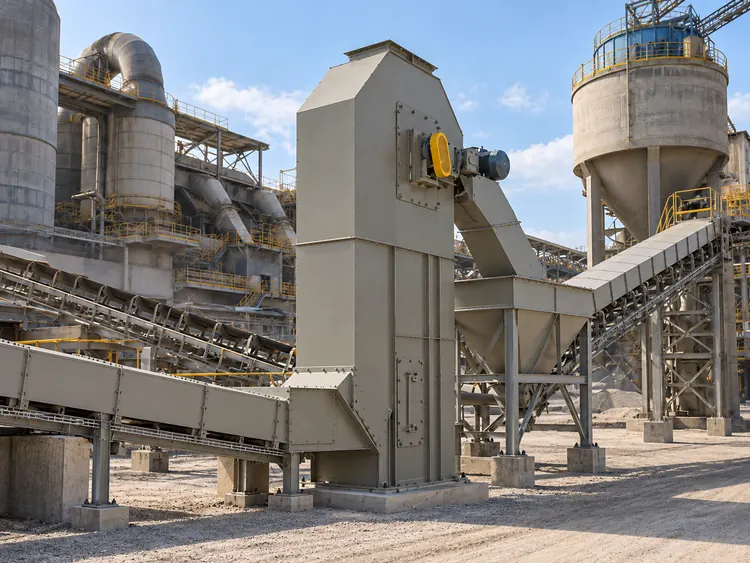 Gray enclosed bucket elevator beside conveyors and silos in a cement plant illustration