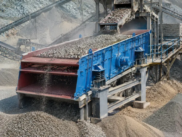 Blue vibrating screen with red discharge sections separating aggregate at an outdoor plant