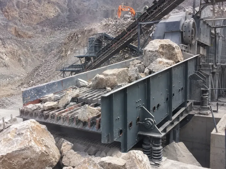 Gray vibrating grizzly feeder carrying large pale rocks in a quarry