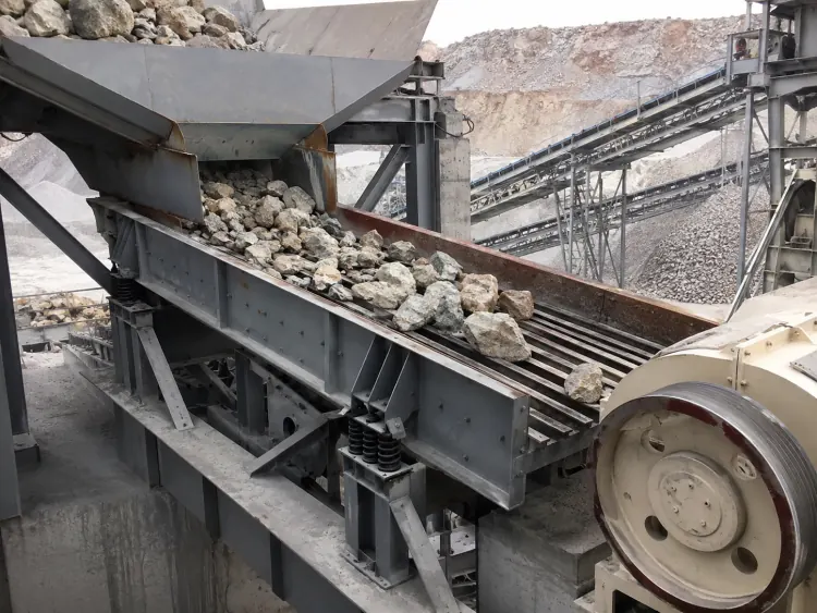 Gray grizzly vibrating feeder delivering rocks into a jaw crusher at a quarry